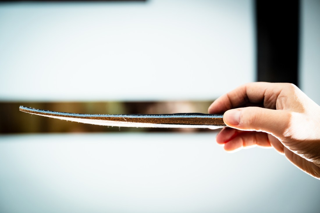 A hand holds the insole by the heel, to show how thin it is.