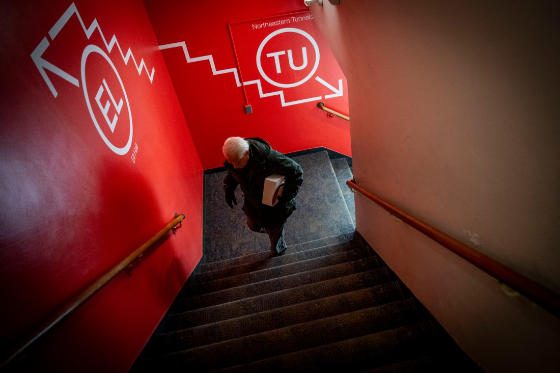 An overhead view of a student ascending a stairwell with bright red walls indicating directional wayfinding to various buildings. 