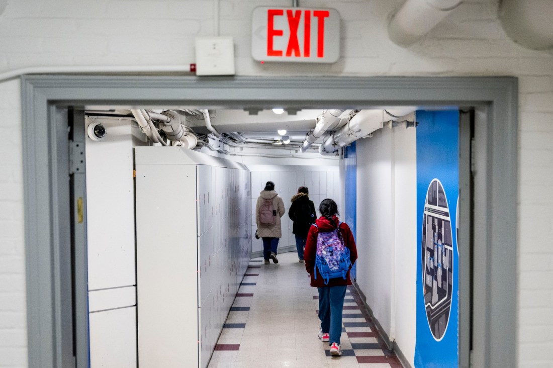 Students walk through the corridors of a brightly lit tunnel with white walls and polished white tile floors. 