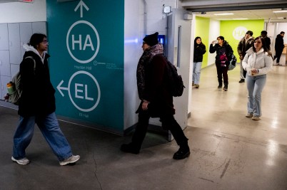 Students walk through a busy hallway intersection in a Northeastern University building, passing a teal wayfinding sign with directional arrows pointing to Hayden Hall (HA) and Ell Hall (EL).