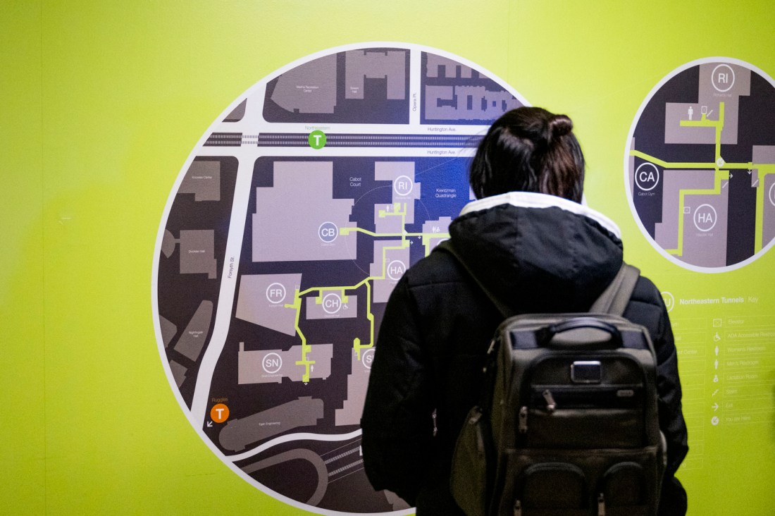 A student wearing a winter coat and a backpack studies the tunnel map on a green background.