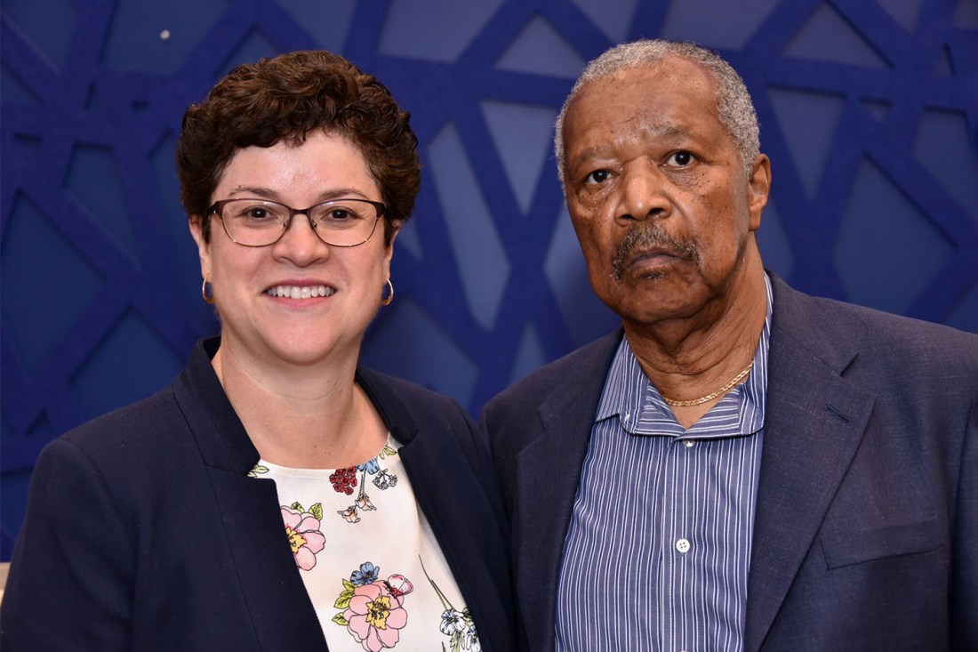 Elmer Freeman wearing a blue striped button down and blazer posing next to Carmen Sceppa, wearing a white shirt with flowers printed on it under a blazer.