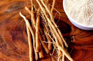 Ashwagandha roots and a white powder known as Withania somnifera in a white bowl on a wooden table.
