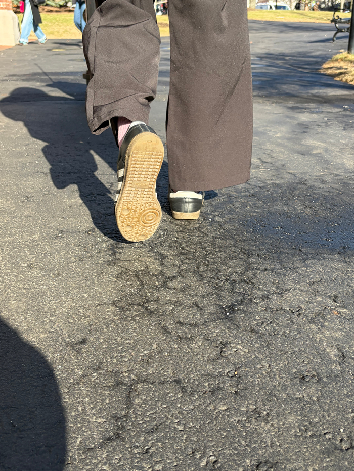 A pair of legs in brown pants walks over pavement.