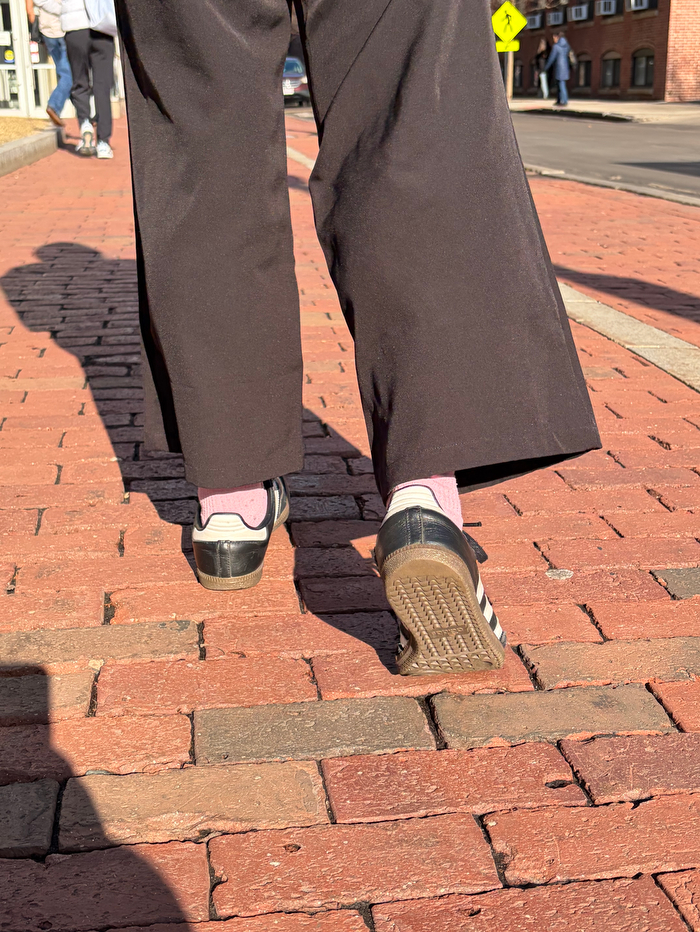 A pair of legs in brown pants walks on bricks.