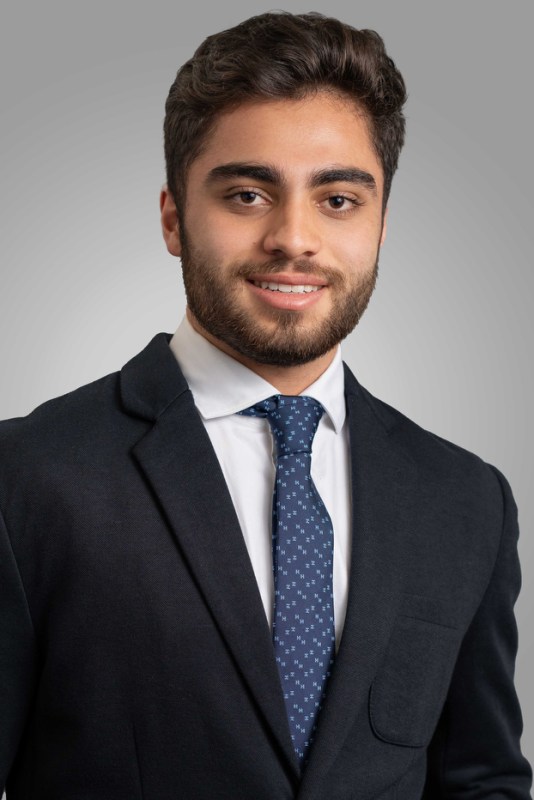 A bearded man wearing a suit and tie (left), a woman wearing a blazer over a white-shirt (center) and another bearded man wearing a blazer and a tie (right).