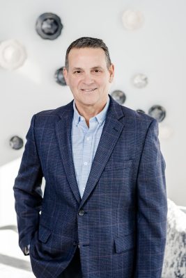 Todd Ruderman, co-founder of the Holocaust Legacy Foundation, stands, smiling, in a blue suit.