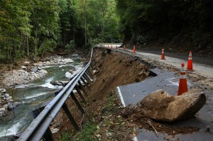 A river rushes by a damaged road with cones on it in Asheville after Hurricane Helene.
