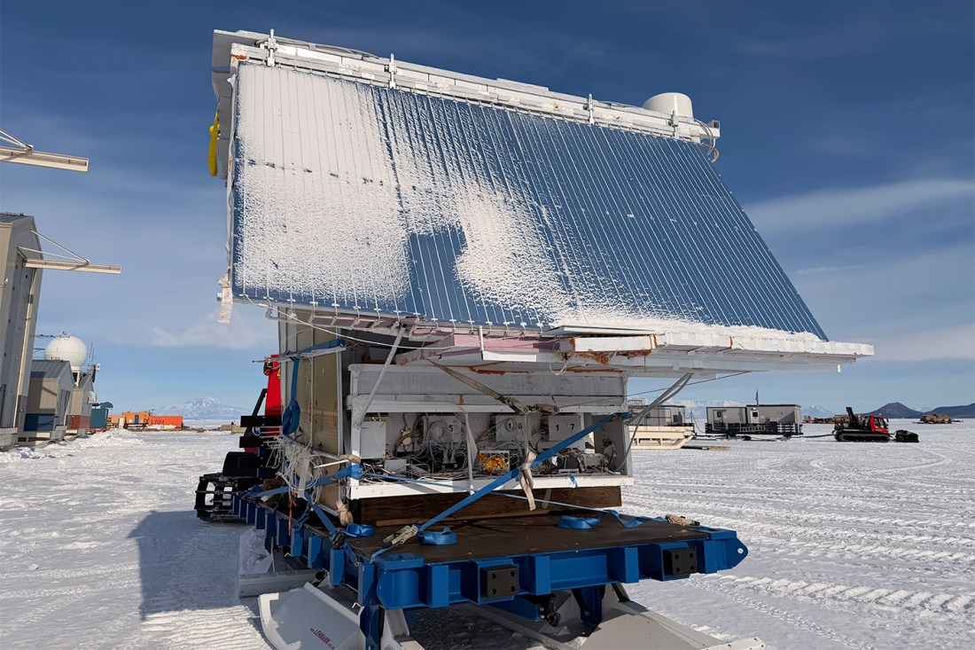 A large detector in the shape of a cube with a larger solar array on one side, on top of a rolling platform in Antarctica.