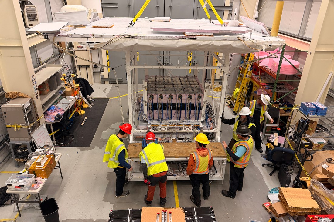 A group of people in yellow vests and hard hats inspect the detector in a warehouse-like room.