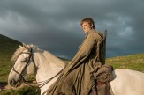 A screen capture from 'A Knight of the Seven Kingdoms' shows a man sitting on top of a white horse, lit by the sun with dark clouds behind him.