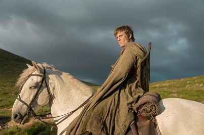 A screen capture from 'A Knight of the Seven Kingdoms' shows a man sitting on top of a white horse, lit by the sun with dark clouds behind him.