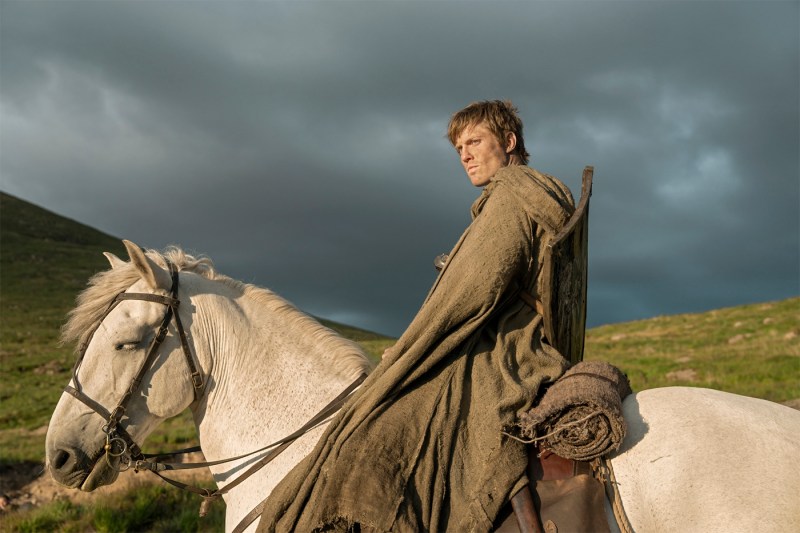 A screen capture from 'A Knight of the Seven Kingdoms' shows a man sitting on top of a white horse, lit by the sun with dark clouds behind him.