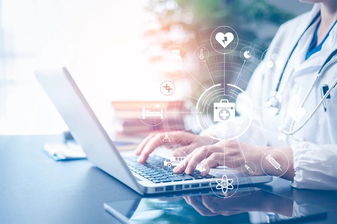 A person in a doctor's coat types on a laptop, while icons hover in the air.