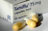 A box of Tamiflu with yellow and white capsules sitting outside of it.