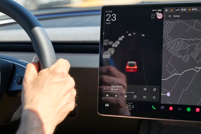 Someone steers a car while their car display shows an icon representing their car and other icons for the other cars. They are also listening to music and going 23 km/h.