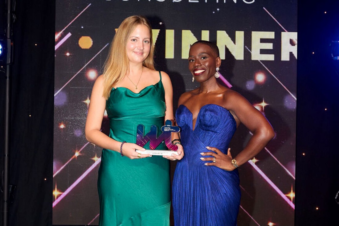 Woman in green dress holds award while woman in blue dress smiles