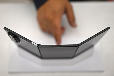 A person points their finger at at a phone with three screens propped up.