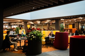 A library space filled with armchairs and tables with students sitting and working at some of them.