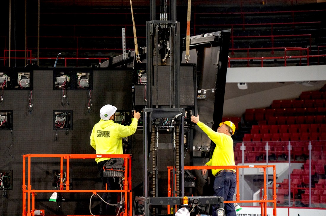 Two workers wearing high-vis yellow shirts and hard hats on orange risers working on shutting Matthews Arena down.