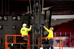Two workers wearing high-vis yellow shirts and hard hats on orange risers working on shutting Matthews Arena down.