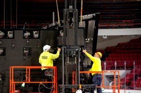 Two workers wearing high-vis yellow shirts and hard hats on orange risers working on shutting Matthews Arena down.