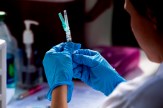 A health professional with gloved hands holding up a syringe and looking at it.