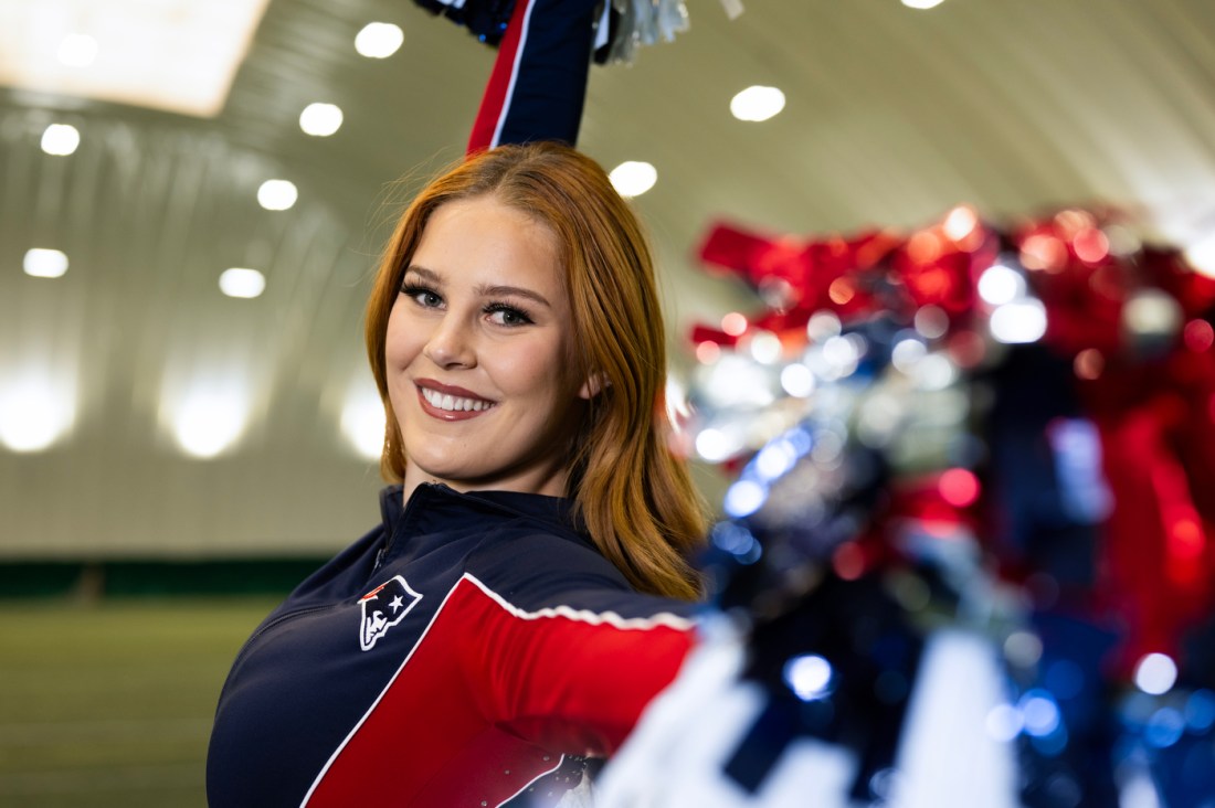 Lana Vogler, smiling and posing with her pom-poms. She's wearing the Patriots Cheerleading uniform.