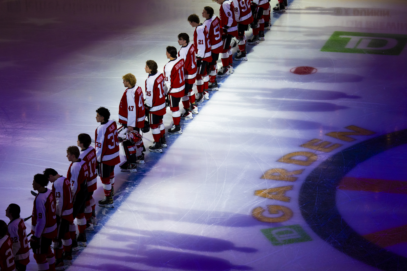 Northeastern players stand shoulder to shoulder along the blue line during pregame ceremonies at TD Garden, illuminated by arena lights.