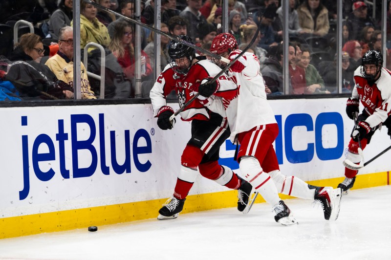 Two hockey players collide into the side of the rink while onlookers watch in the crowd.