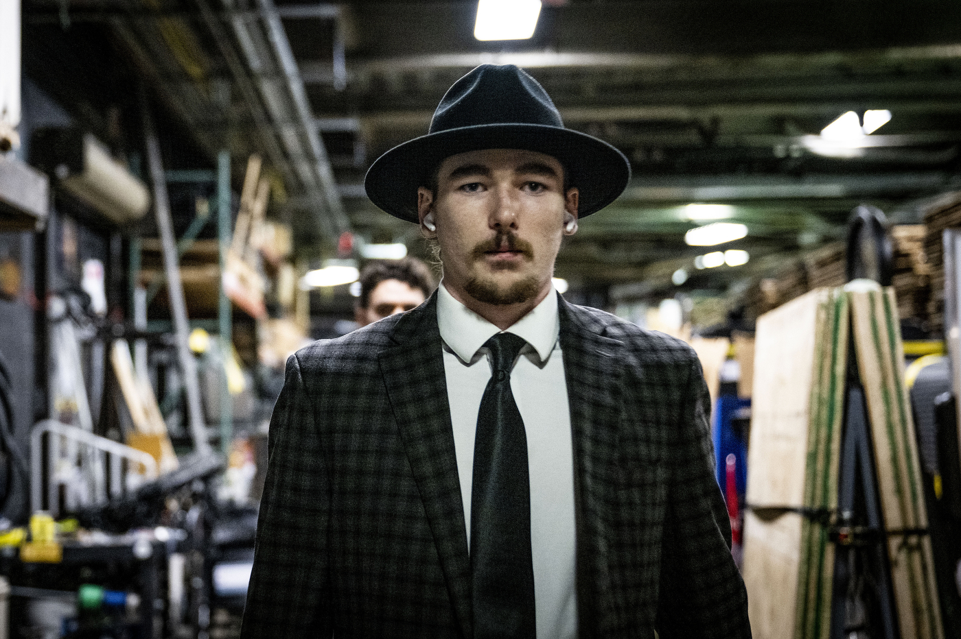 A Northeastern player wearing a black fedora-style hat and suit walks alone through a narrow backstage corridor beneath TD Garden.