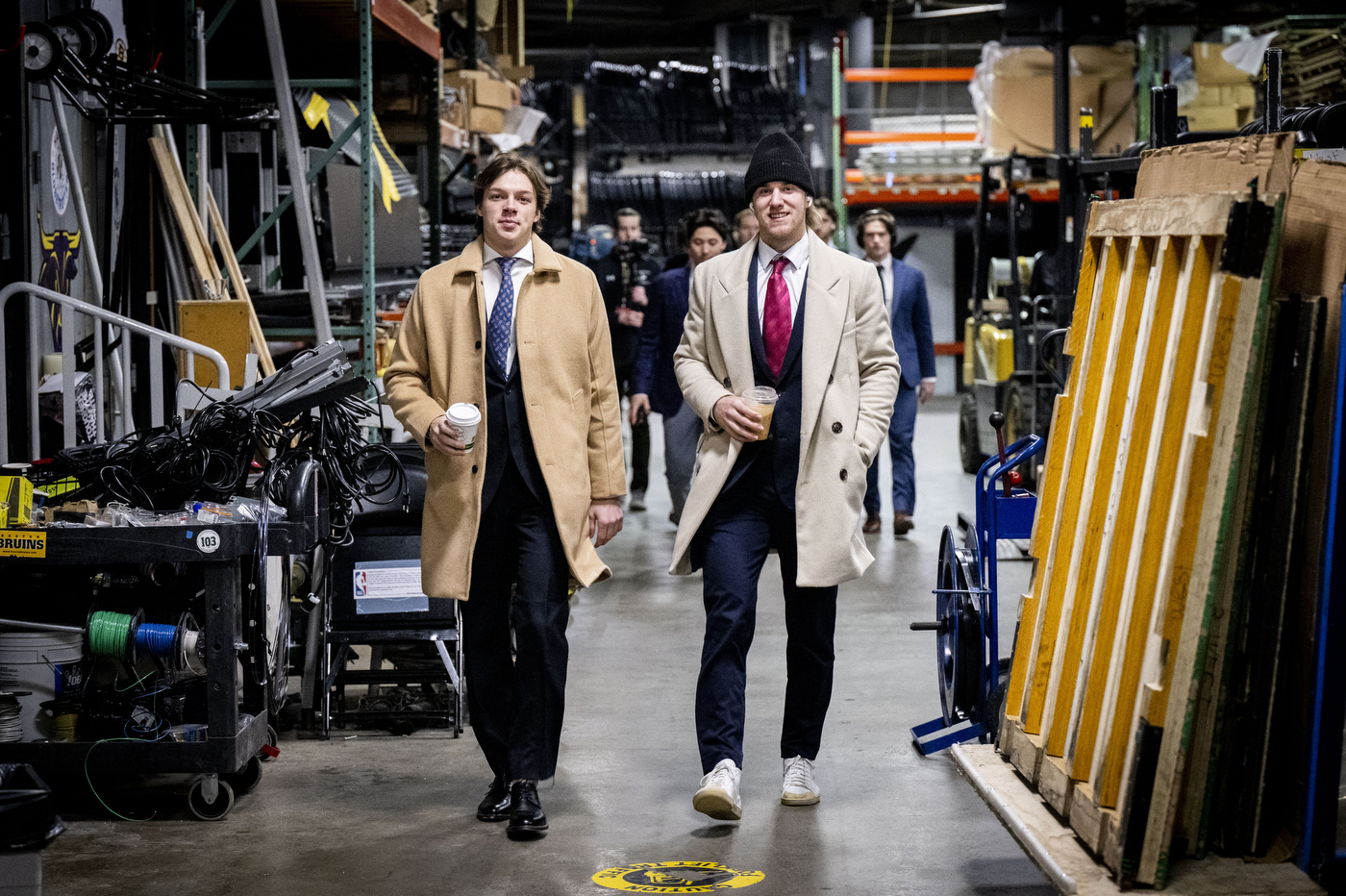 Two Northeastern players in suits and coats walk confidently through an equipment-filled arena hallway on their way to the Beanpot semifinal at TD Garden.