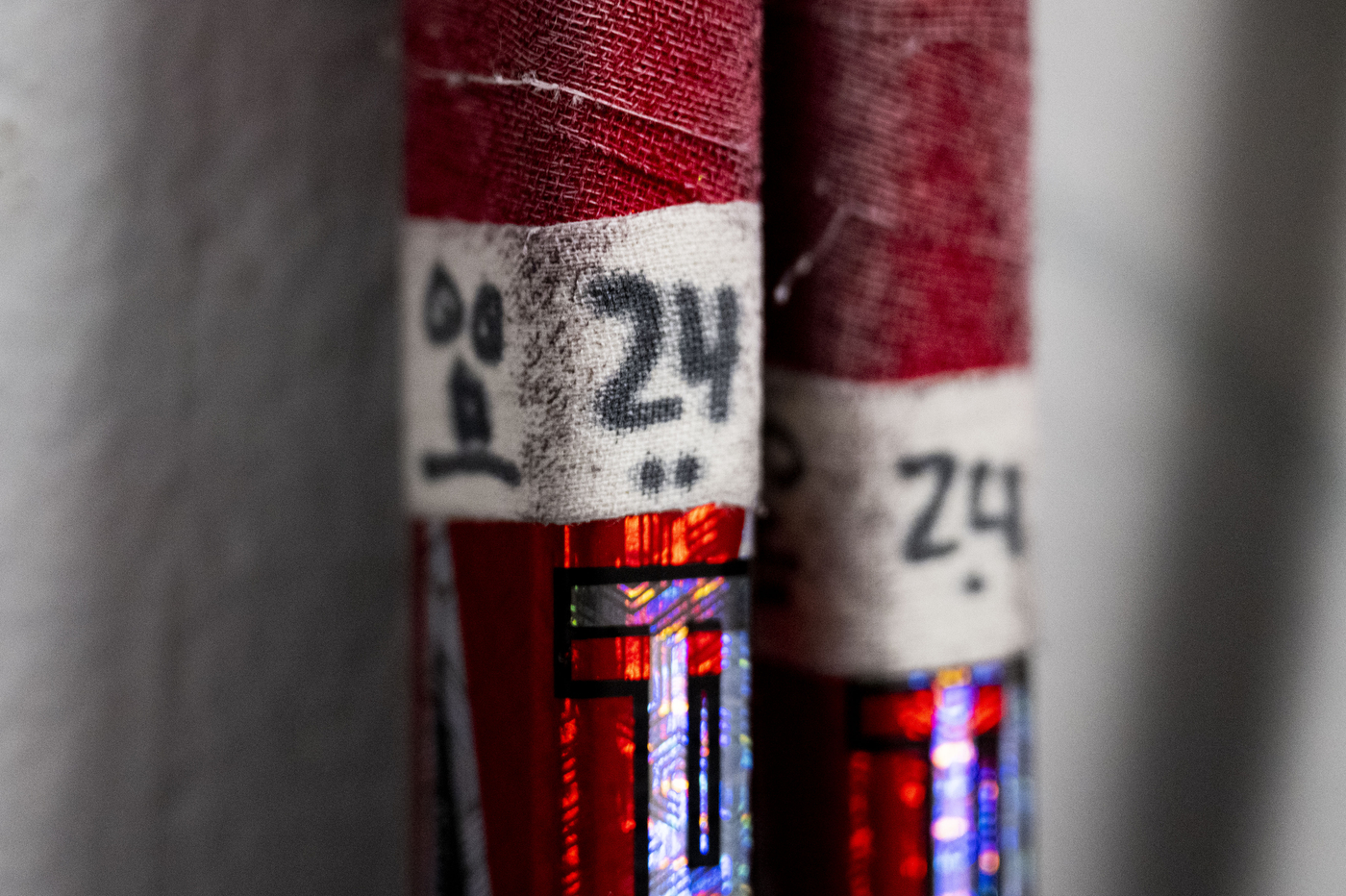 Close-up of red-and-white taped hockey sticks lined up vertically, showing worn fabric, numbering, and reflective detailing.