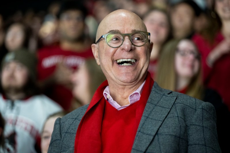 The university president smiles while wearing glasses, blurred out members of the crowd behind him.
