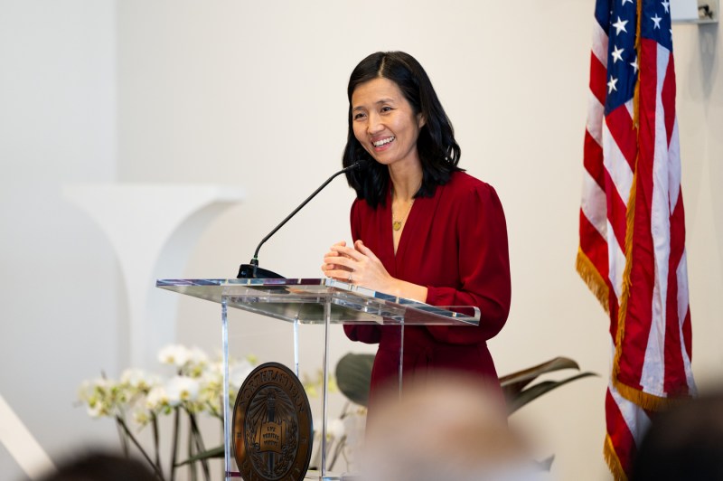 The mayor of Boston, dressed in red stands, at a podium while speaking into the microphone.