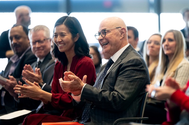 The mayor of Boston and university president applaud while sitting next to each other during an event.