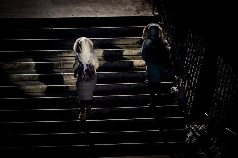 Two people wearing puffer coats back the camera as they walk up stairs on the Boston campus.