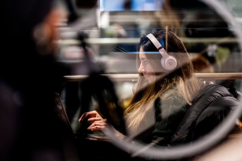 A person wearing headphones sits in Snell Library while using a laptop.