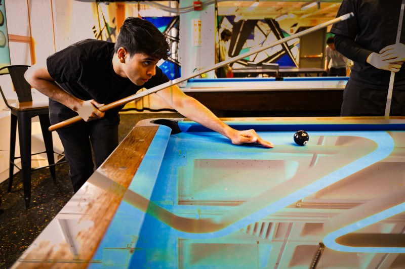 A person holding a pool stick prepares leans on a pool table.