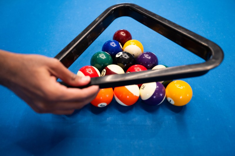 A hand holds a ball rack while re-racking pool balls.