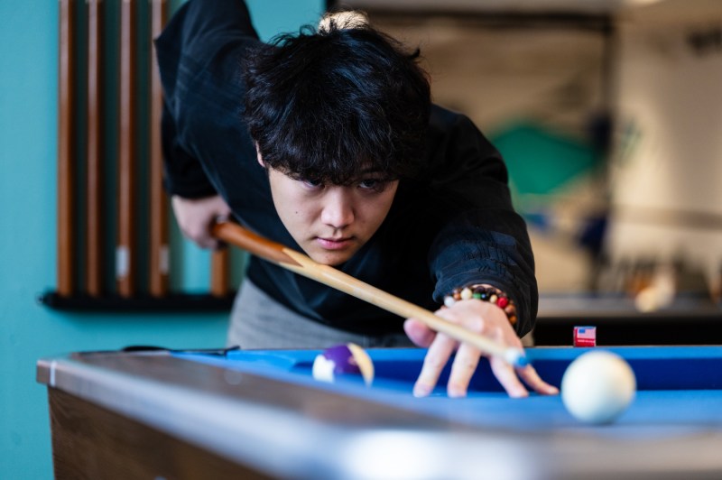 A closeup on the face of a student playing pool as he lines up a shot.