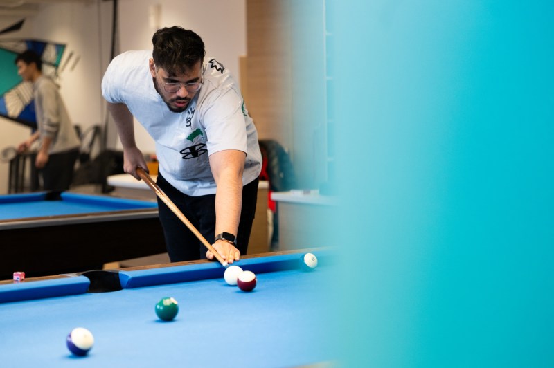 A person leans over a pool table holding a pool stick, lining up a shot on the 8 ball.