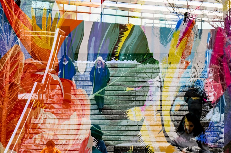 A camera effect overlays a painted mural on two people walking down snow-covered stairs on the Boston campus.
