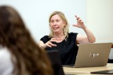 A woman in a black blouse gestures while teaching with a laptop open in front of her.