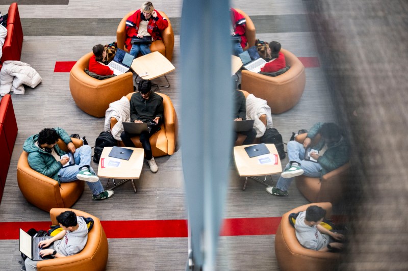 Students sit on curved armchairs while doing work. Some use laptops. 