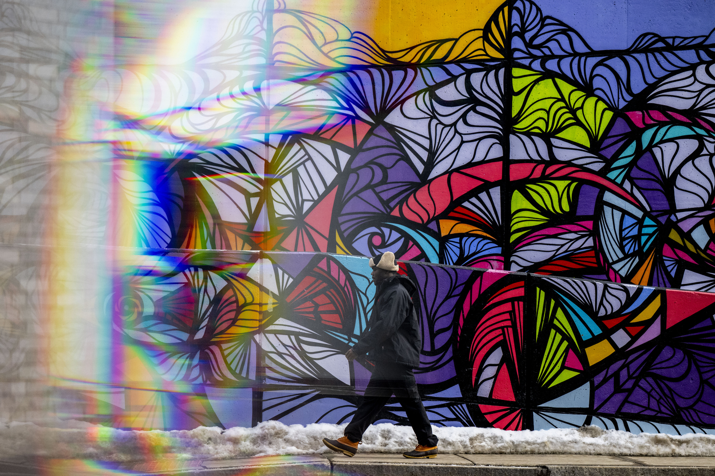 A person wearing a winter hat walks past a colorful mural on the Boston campus. 