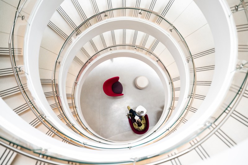 A member of the Northeastern community is seen siting on a chair in ISEC, through the spiral staircase.