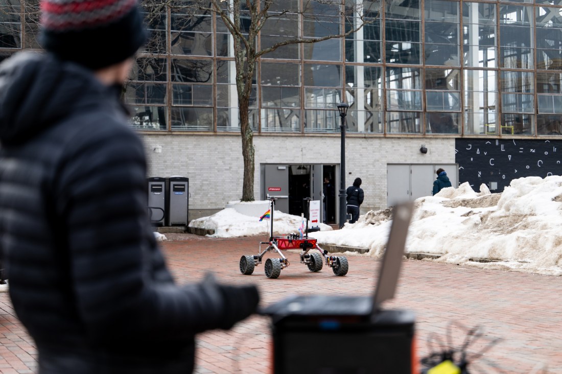 A student works on a robot outside. The robot is seen in the background. 