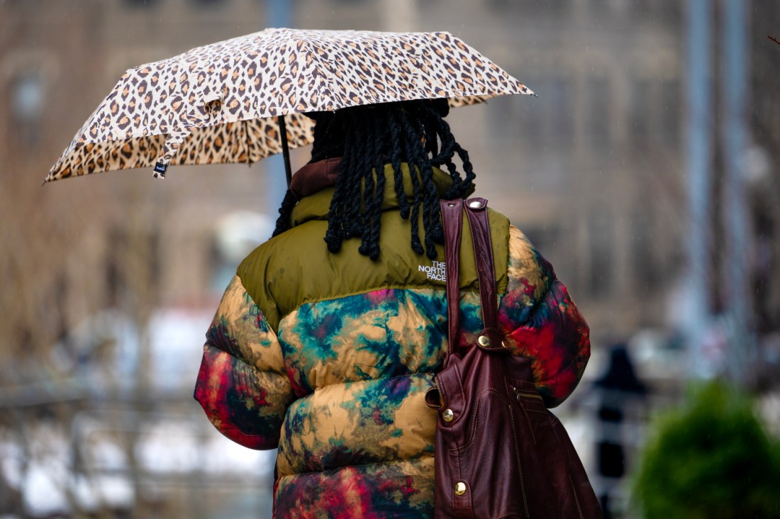 A person with their back to the camera walks through the Boston campus while holding a cheetah print umbrella.