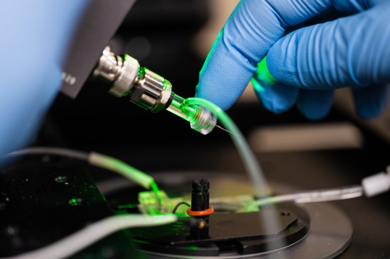 A close-up of gloved hands routing wires on a laser device in a laboratory.